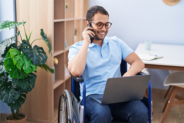 A man in a wheelchair using a laptop and talking on the phone while managing receivables.