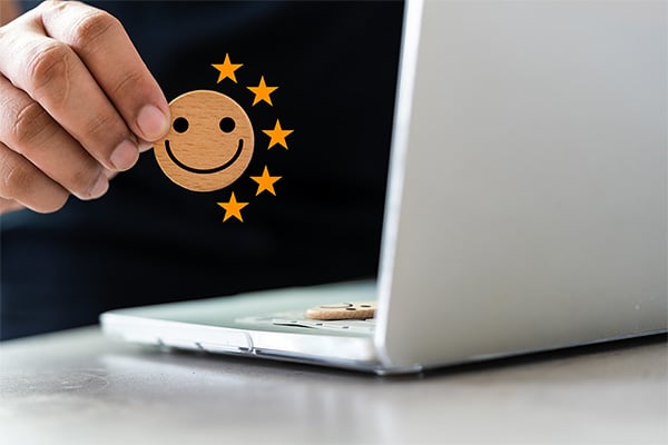 A person holding a smiley face sticker on a laptop as part of a marketing campaign.
