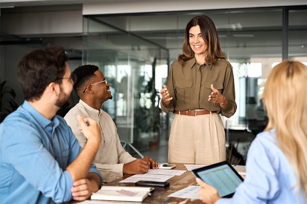 Group of professionals having a meeting in an office setting, with one woman standing and speaking to the others.