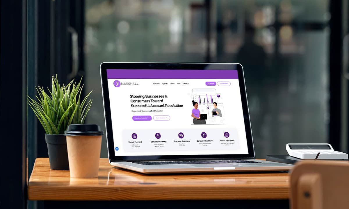 A laptop on a wooden table displaying a website with the brand name 'Marshall,' featuring a purple-themed design and options related to consumer and business account resolution. A small potted plant and a takeaway coffee cup are also on the table.