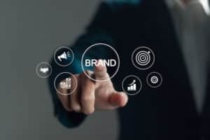 Person in a suit touching a digital interface with the word 'BRAND' surrounded by icons representing marketing and business concepts.