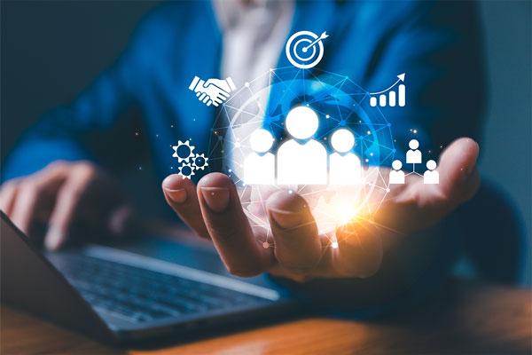 A person in a suit uses a laptop while holding up a digital illustration of business-related icons, including people, a target, handshake, and graph, symbolizing networking and business strategy.